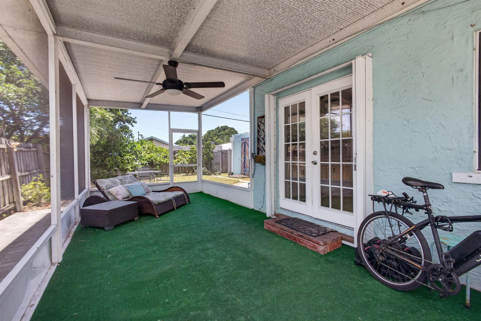 A covered screened-in porch features green turf flooring, a ceiling fan, and a bicycle — 1314 N J Street, FL 33460, FL
