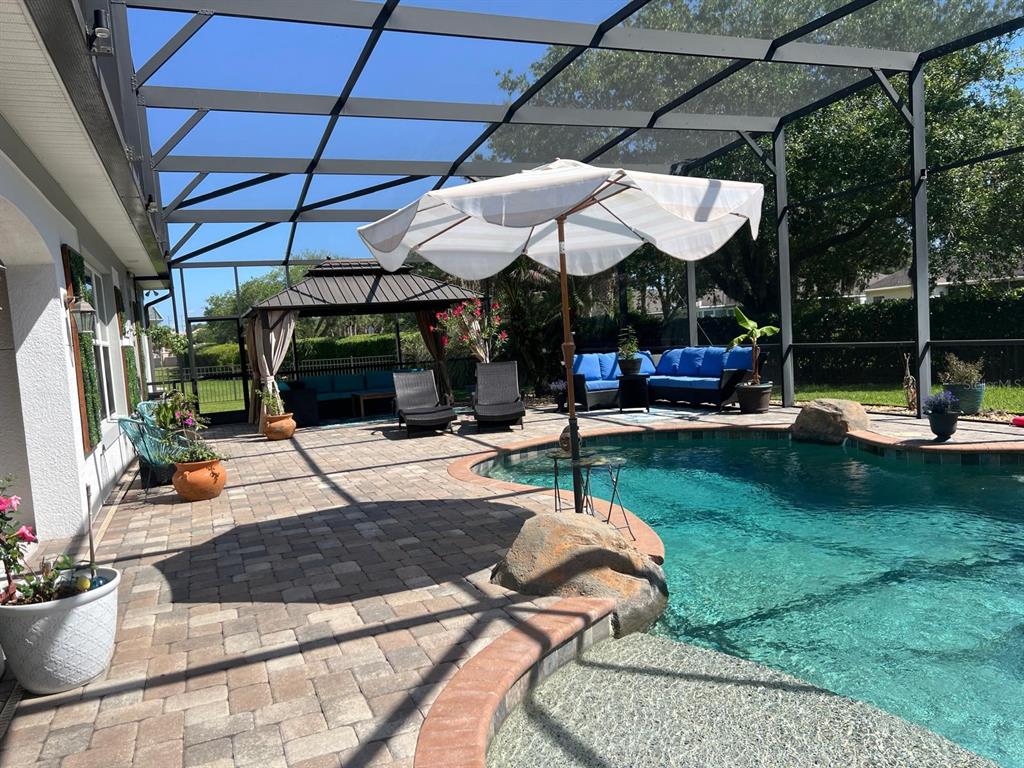 A screened-in patio features a swimming pool, a gazebo, and outdoor furniture on pavers — 12 LIONSPAW GRAND, DAYTONA BEACH, FL