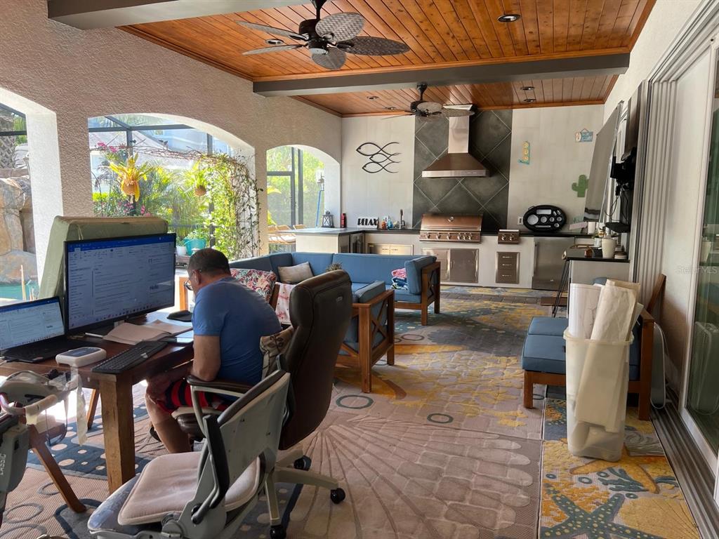 A covered outdoor patio features a kitchen, seating area, and a person working at a desk — 12 LIONSPAW GRAND, DAYTONA BEACH, FL