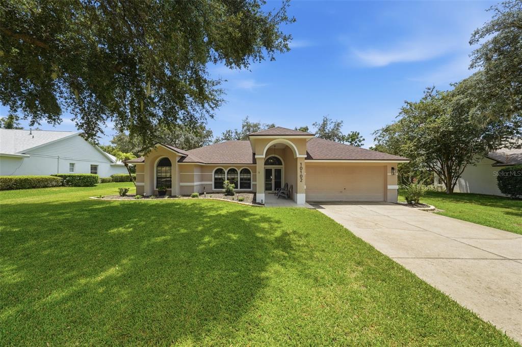 A single-story house with a beige stucco exterior, a two-car garage, and a large lawn — 10102 SILVER BLUFF DRIVE, LEESBURG, FL