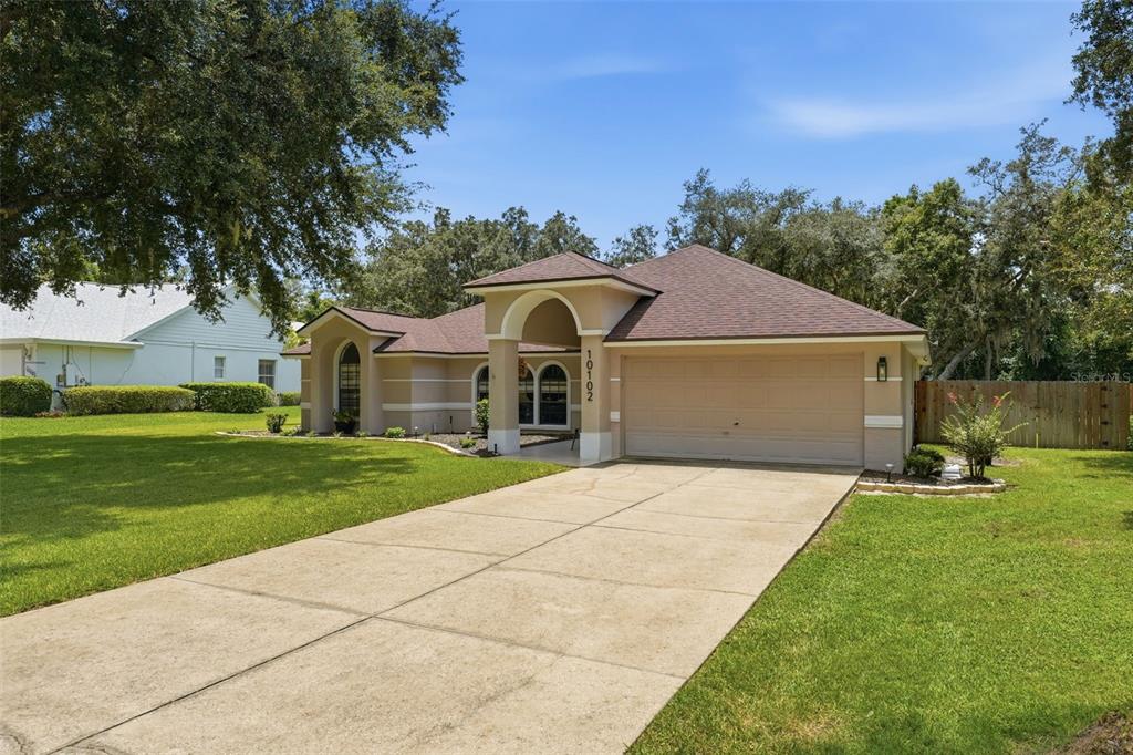 A single-story house with a beige exterior, a two-car garage, and a concrete driveway — 10102 SILVER BLUFF DRIVE, LEESBURG, FL