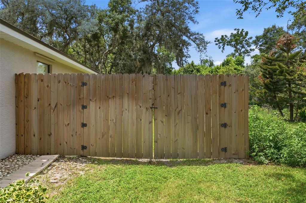 A wooden privacy fence with a double gate stands next to the side of a house — 10102 SILVER BLUFF DRIVE, LEESBURG, FL