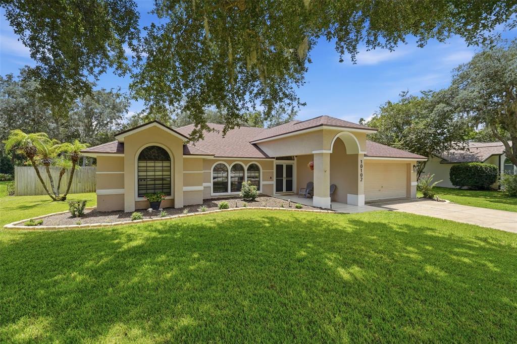 A single-story house with a tan stucco exterior, a brown roof, and a two-car garage — 10102 SILVER BLUFF DRIVE, LEESBURG, FL