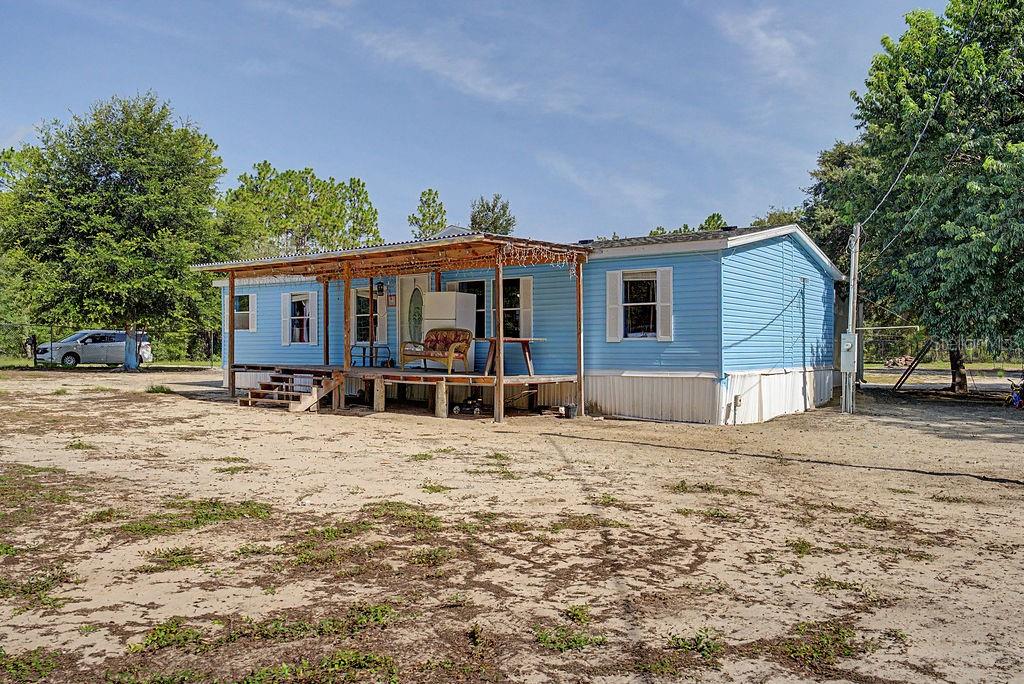 A light blue single-wide mobile home with a wooden porch sits on a sandy lot — 7491 NE 101ST COURT, BRONSON, FL