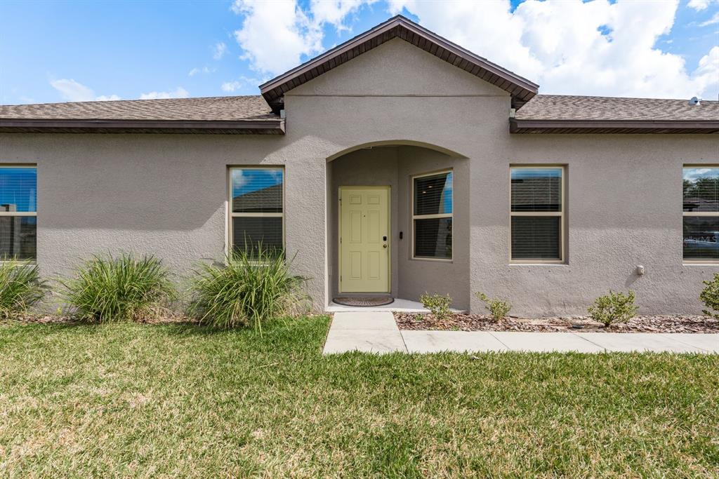 The exterior of a single-story house features a light yellow front door and stucco walls — 13387 CREST LAKE DRIVE, HUDSON, FL