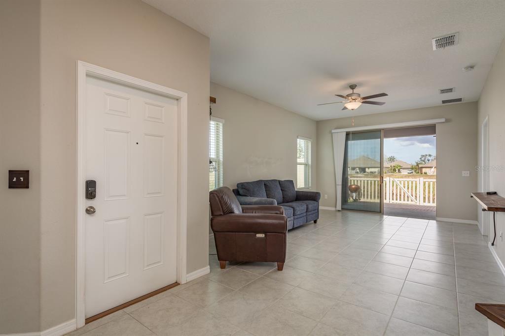 A living room with tile flooring, a brown leather chair, a blue sofa, and sliding doors — 13387 CREST LAKE DRIVE, HUDSON, FL