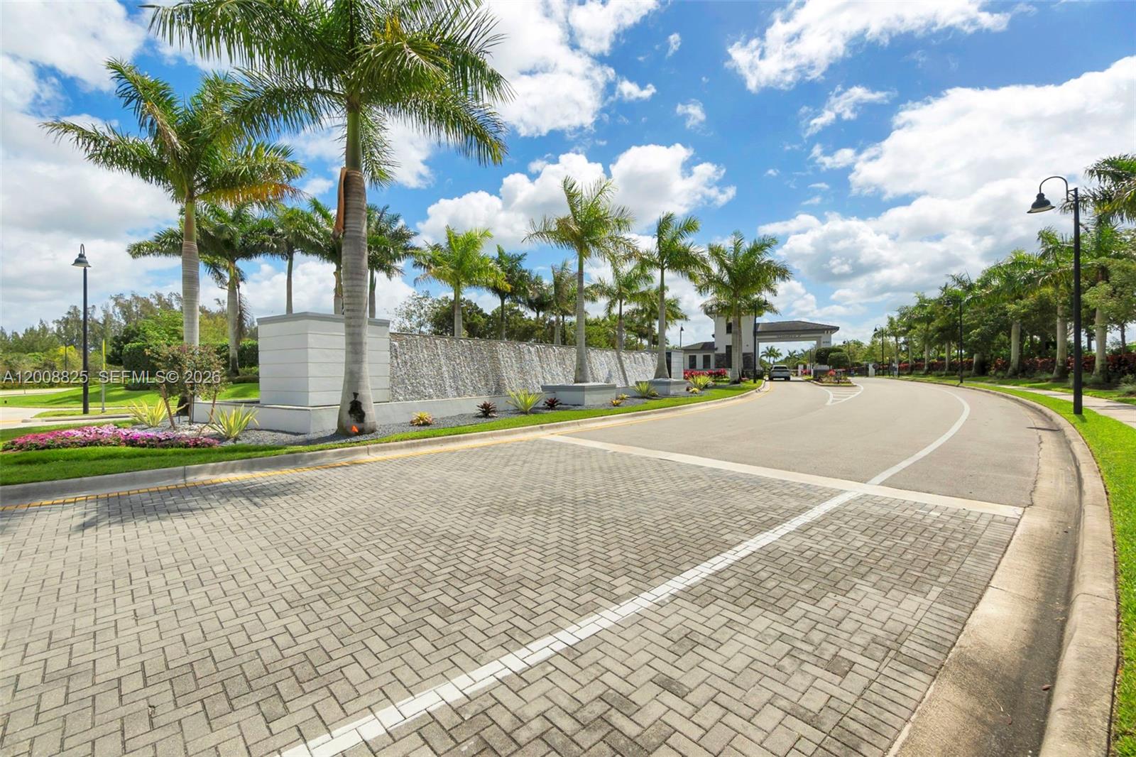 A paved entrance road leads toward a gated community with a decorative water feature — 8022 Deer Lake Ct, Parkland FL 33067, PARKLAND, FL