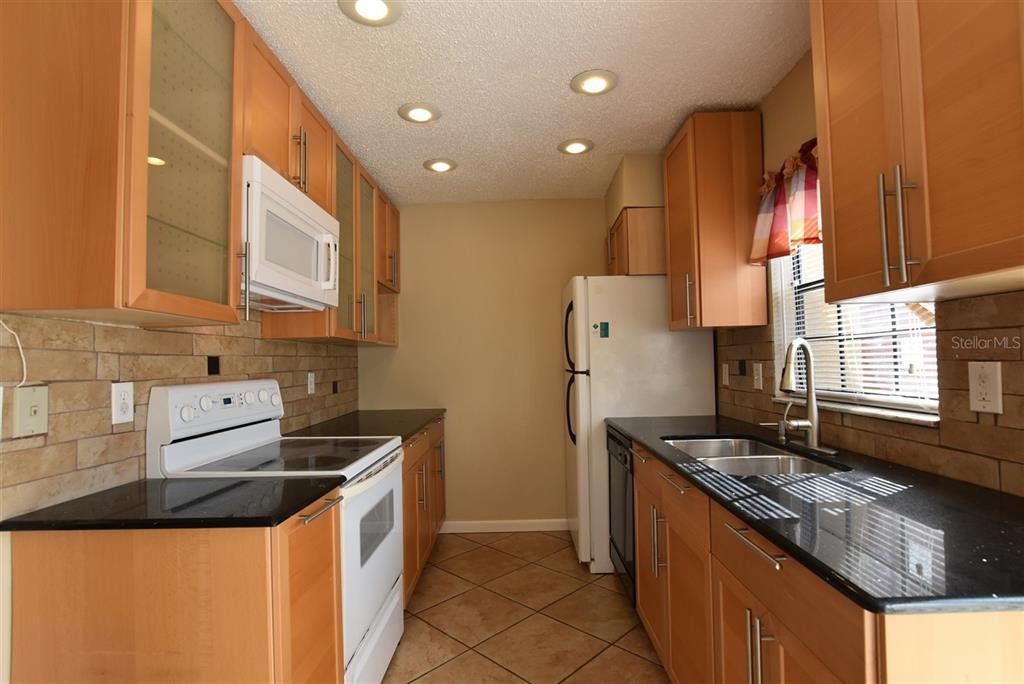 A galley kitchen features light wood cabinets, black countertops, a white stove, and tiled floors — 3374 CEDAR SPRINGS PLACE UNIT 155, WINTER PARK, FL