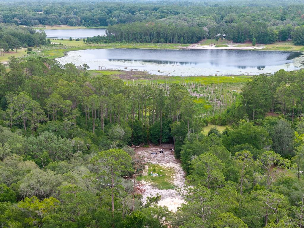 An aerial view shows a cleared sandy lot surrounded by dense forest near a lake — 261 ASHLEY LAKE DRIVE, MELROSE, FL