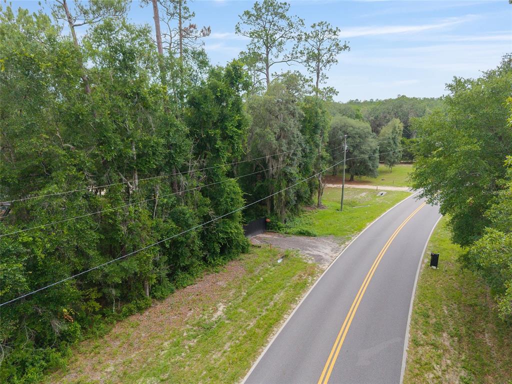 An aerial view shows a paved road curving past a wooded lot with power lines — 261 ASHLEY LAKE DRIVE, MELROSE, FL