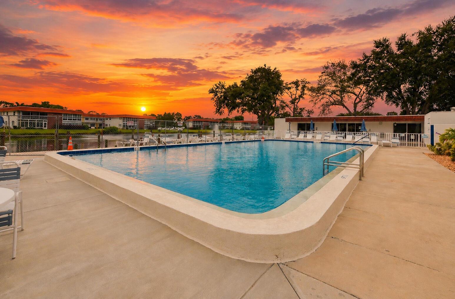 A rectangular swimming pool sits on a concrete deck at sunset near apartment buildings — 1225 NW 21st Street # 311, Stuart FL 34994, STUART, FL
