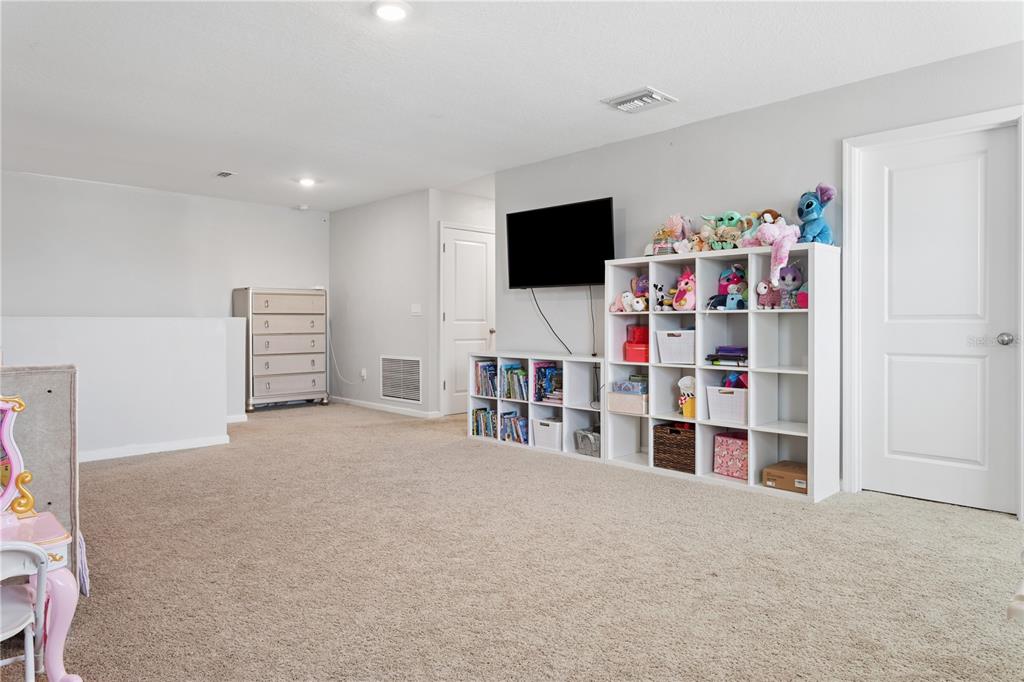 A carpeted playroom features a wall-mounted television, white shelving units, and a dresser — 35159 DAISY MEADOW LOOP, ZEPHYRHILLS, FL