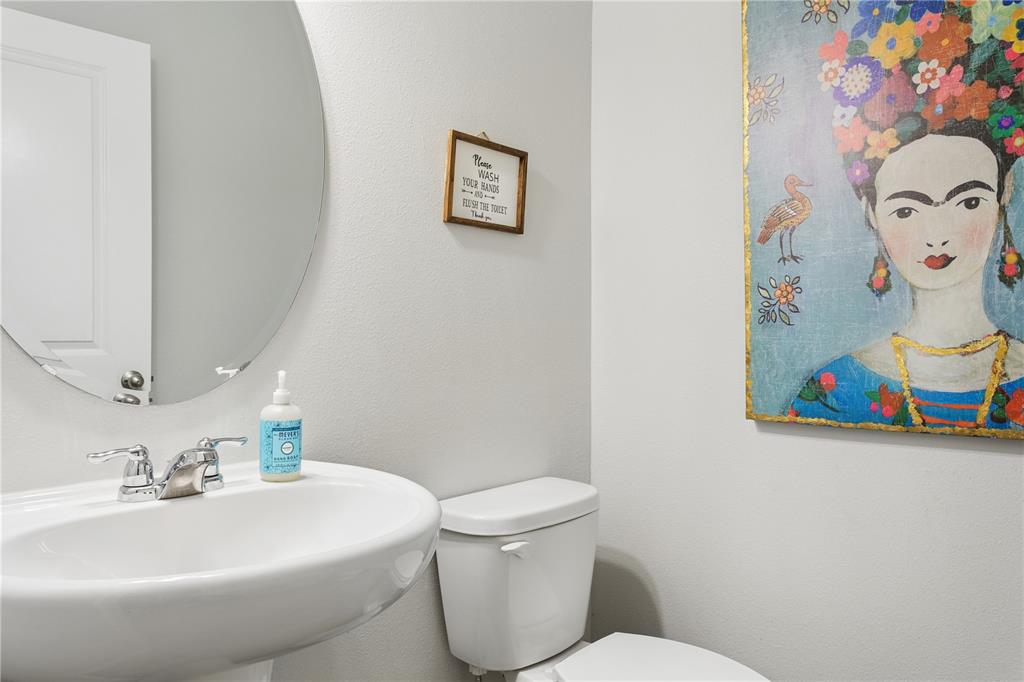 A powder room features a pedestal sink, a round mirror, and a colorful Frida Kahlo painting — 35159 DAISY MEADOW LOOP, ZEPHYRHILLS, FL