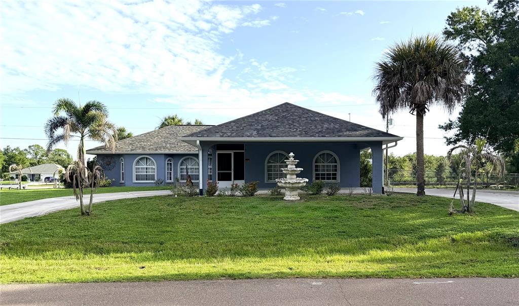 A blue single-story house with a large front lawn, a fountain, and palm trees — 22262 SEYBURN TERRACE, PORT CHARLOTTE, FL