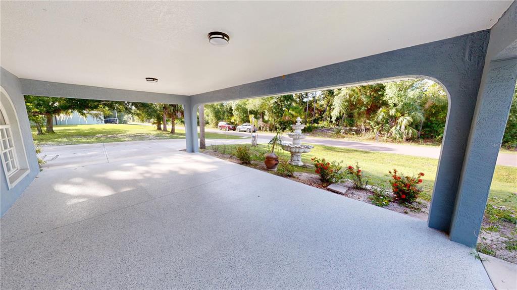 A covered concrete carport features a decorative fountain and landscaping in the front yard — 22262 SEYBURN TERRACE, PORT CHARLOTTE, FL