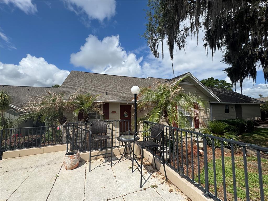 A patio with a metal railing, two chairs, and a small table faces a house — 1106 VILLA LANE UNIT 81, APOPKA, FL