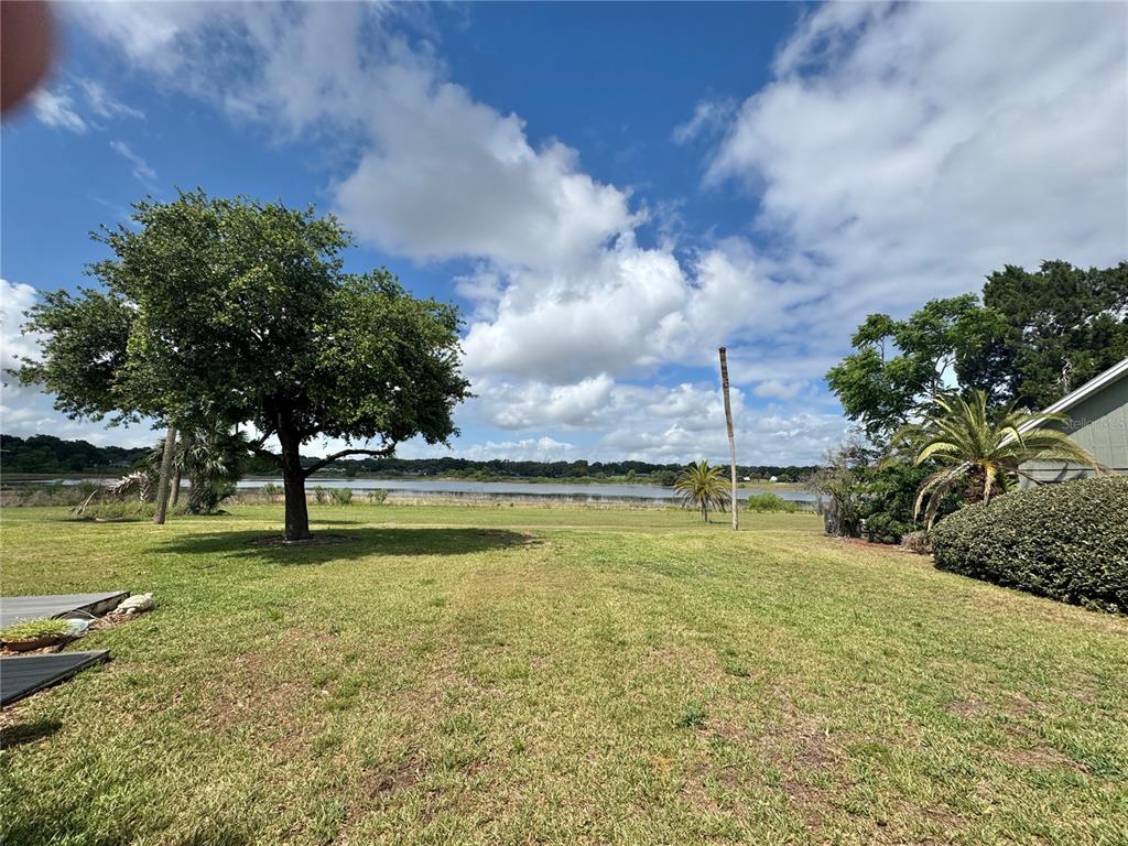 A grassy backyard overlooks a lake under a blue sky with scattered clouds — 1106 VILLA LANE UNIT 81, APOPKA, FL