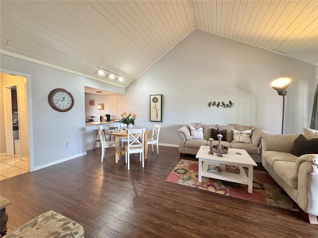 A living and dining area features vaulted ceilings, wood-look flooring, and neutral-toned furniture — 1106 VILLA LANE UNIT 81, APOPKA, FL