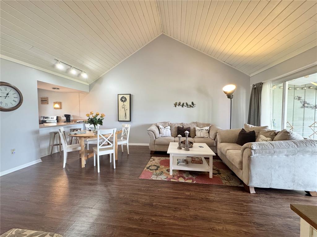 A living room and dining area with vaulted wood ceilings, dark flooring, and neutral furniture — 1106 VILLA LANE UNIT 81, APOPKA, FL
