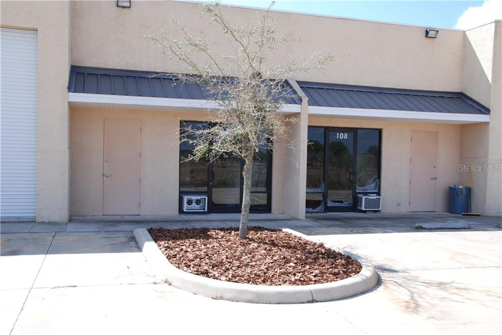 The exterior of a commercial building features two glass entryways, metal awnings, and a tree — 28041 AIRPARK DRIVE UNIT 123,121,115,110,101, PUNTA GORDA, FL