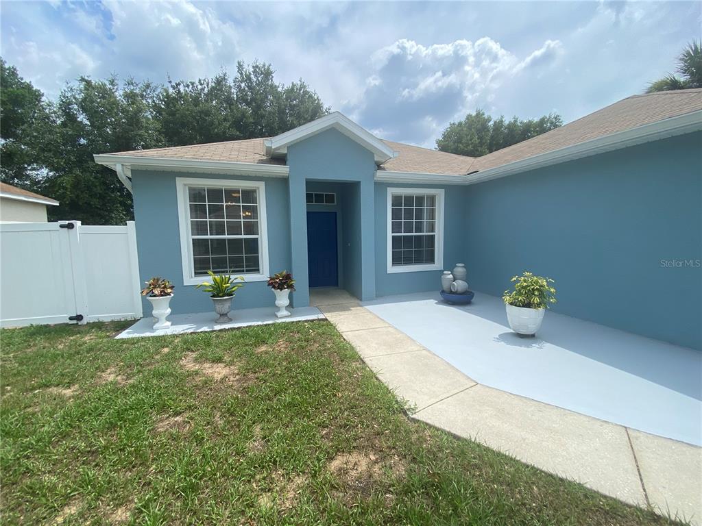 A blue house exterior features a front walkway, a blue door, and several potted plants — 302 BLUFF PASS DRIVE, EUSTIS, FL