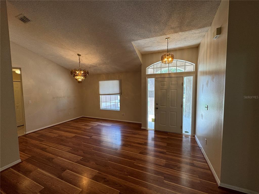 An empty room with wood-look flooring, vaulted ceilings, two chandeliers, and a front entryway door — 302 BLUFF PASS DRIVE, EUSTIS, FL