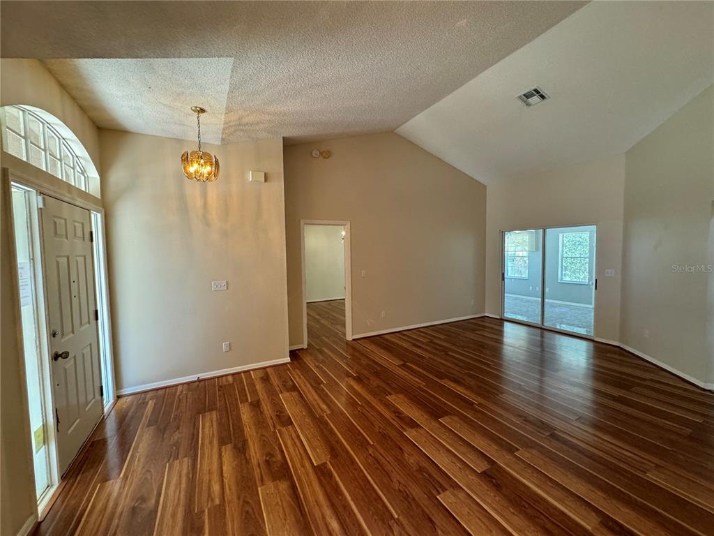 An empty living room features vaulted ceilings, dark wood flooring, and a glass sliding door — 302 BLUFF PASS DRIVE, EUSTIS, FL