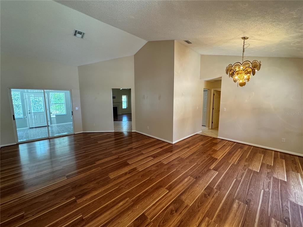 A living room with vaulted ceilings, wood-look flooring, and a large multi-tiered chandelier — 302 BLUFF PASS DRIVE, EUSTIS, FL