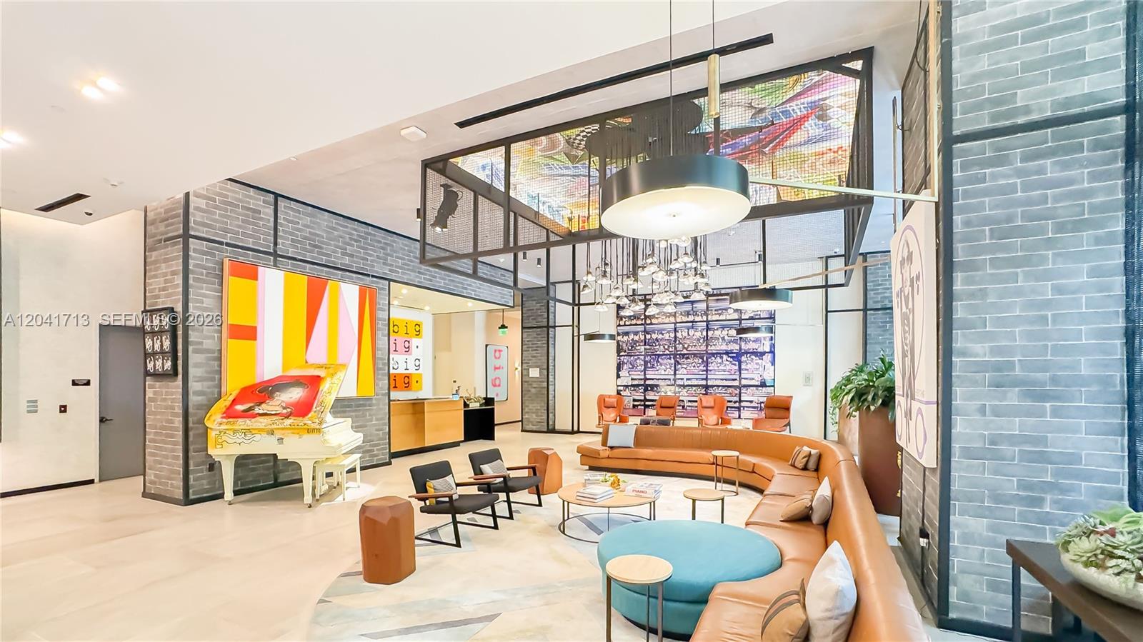 A modern lobby features a curved leather sofa, a white piano, and decorative brick walls — 121 NE 34th St # 814, Miami FL 33137, MIAMI, FL