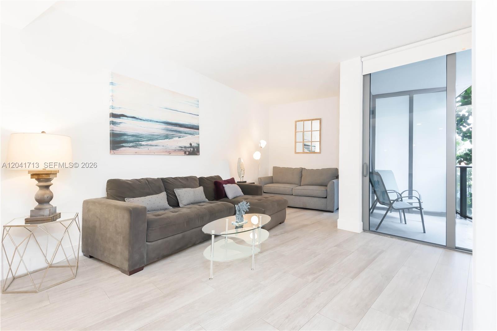 A living room features a sectional sofa, a glass coffee table, and a sliding glass door — 121 NE 34th St # 814, Miami FL 33137, MIAMI, FL