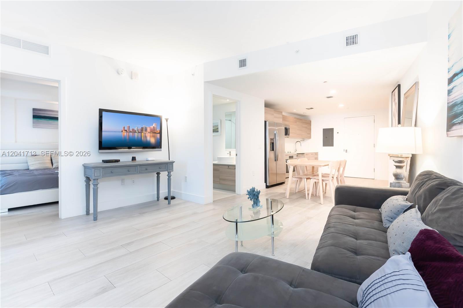 A living room with a grey sofa, glass coffee table, and an adjacent open kitchen — 121 NE 34th St # 814, Miami FL 33137, MIAMI, FL