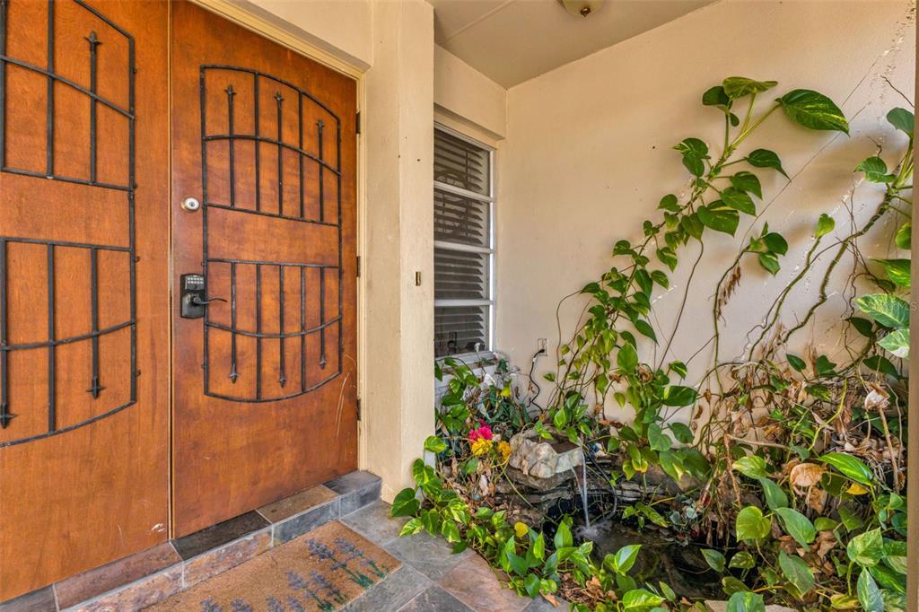 A wooden double door entrance features a small stone water fountain and climbing green vines — 18 ANNAPOLIS LANE, ROTONDA WEST, FL