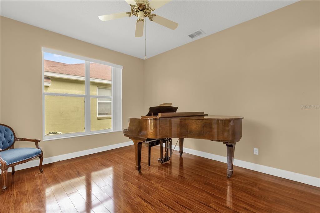 A room with hardwood floors, a grand piano, a ceiling fan, and a blue chair — 5653 MAGNOLIA BLOOM TERRACE, OVIEDO, FL