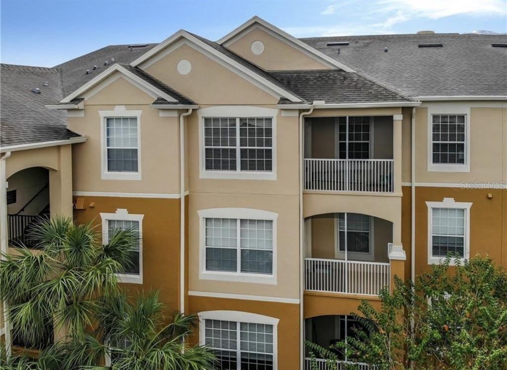 An exterior view of a multi-story apartment building with tan stucco walls and screened balconies — 6434 CAVA ALTA DRIVE UNIT 304, ORLANDO, FL
