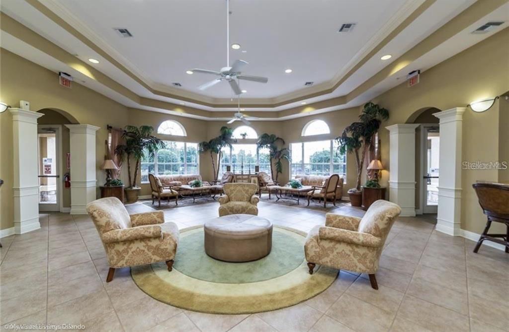 A spacious community clubhouse lounge features tiled floors, a central seating area, and large windows — 6434 CAVA ALTA DRIVE UNIT 304, ORLANDO, FL