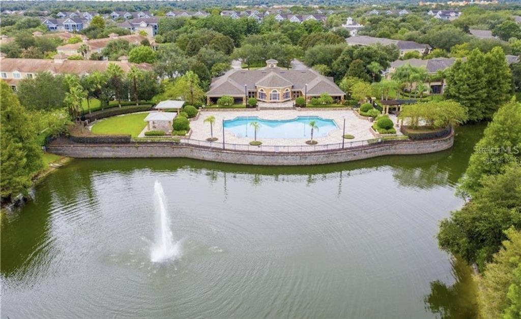 An aerial view shows a community clubhouse with a pool and fountain overlooking a lake — 6434 CAVA ALTA DRIVE UNIT 304, ORLANDO, FL