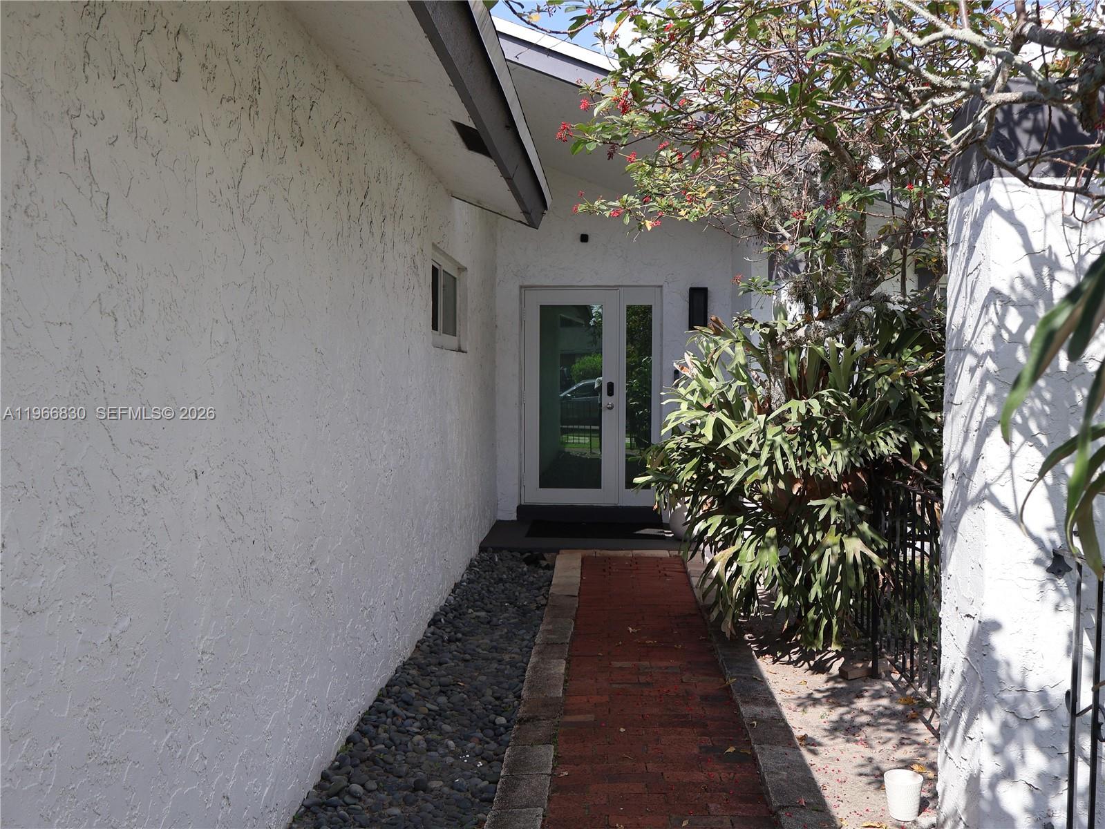 A brick walkway leads to a white front door beside a large staghorn fern — 5505 SW 9th St # 0, Margate FL 33068, MARGATE, FL
