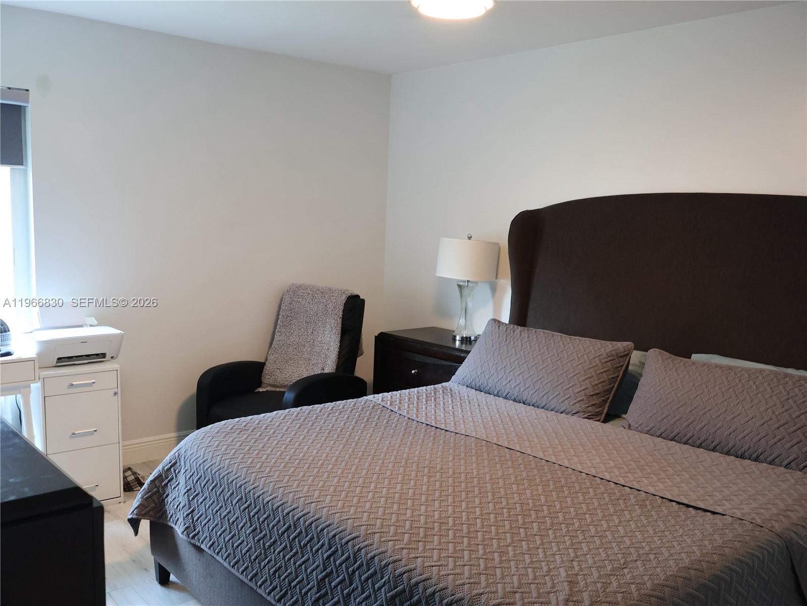 A bedroom features a dark upholstered bed, a nightstand with a lamp, and a chair — 5505 SW 9th St # 0, Margate FL 33068, MARGATE, FL