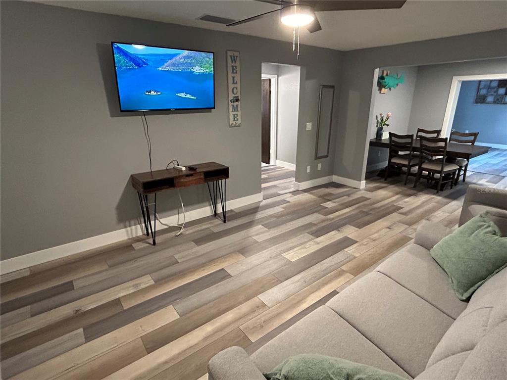 A living room features gray walls, wood-look flooring, a wall-mounted television, and a ceiling fan — 5702 27TH AVENUE S, GULFPORT, FL