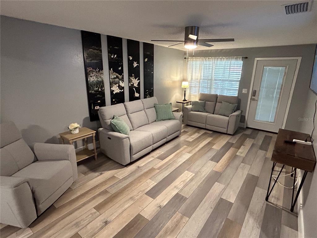 A living room features light gray furniture, wood-look flooring, and a four-panel wall art piece — 5702 27TH AVENUE S, GULFPORT, FL