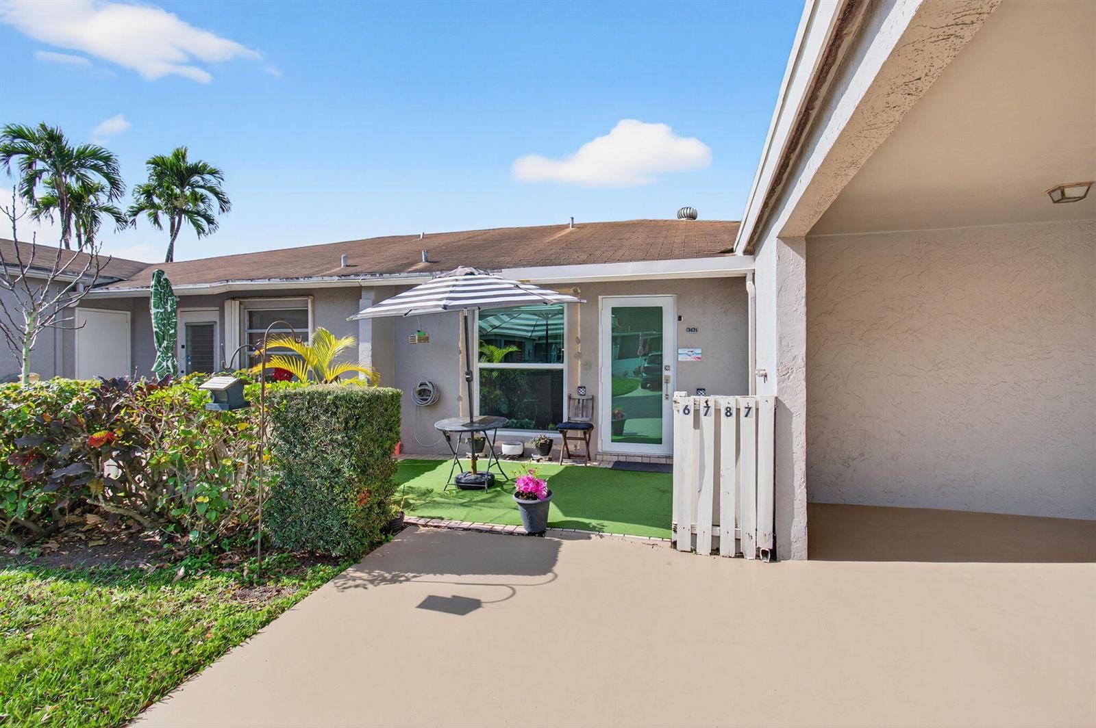 A patio with artificial turf, a small table, and an umbrella sits before a house entrance — 6787 Moonlit Drive, Delray Beach FL 33446, DELRAY BEACH, FL
