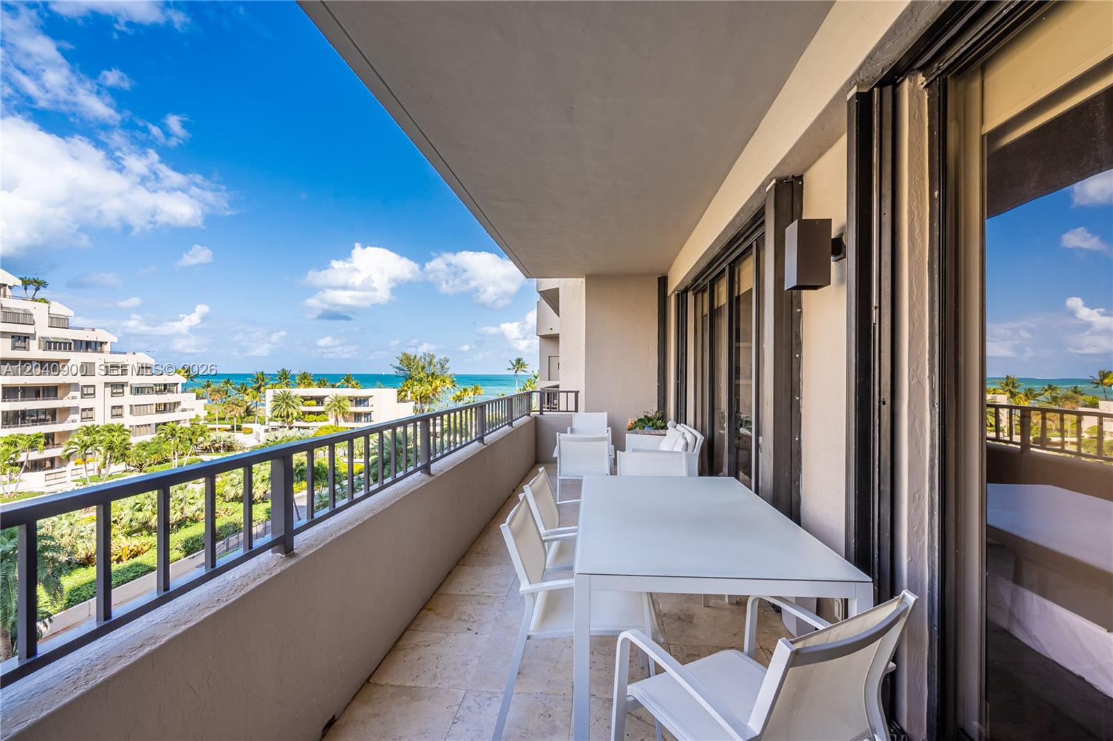 A balcony with a dining set overlooks a tropical landscape and the ocean — 201 Crandon Blvd # 530, Key Biscayne FL 33149, KEY BISCAYNE, FL