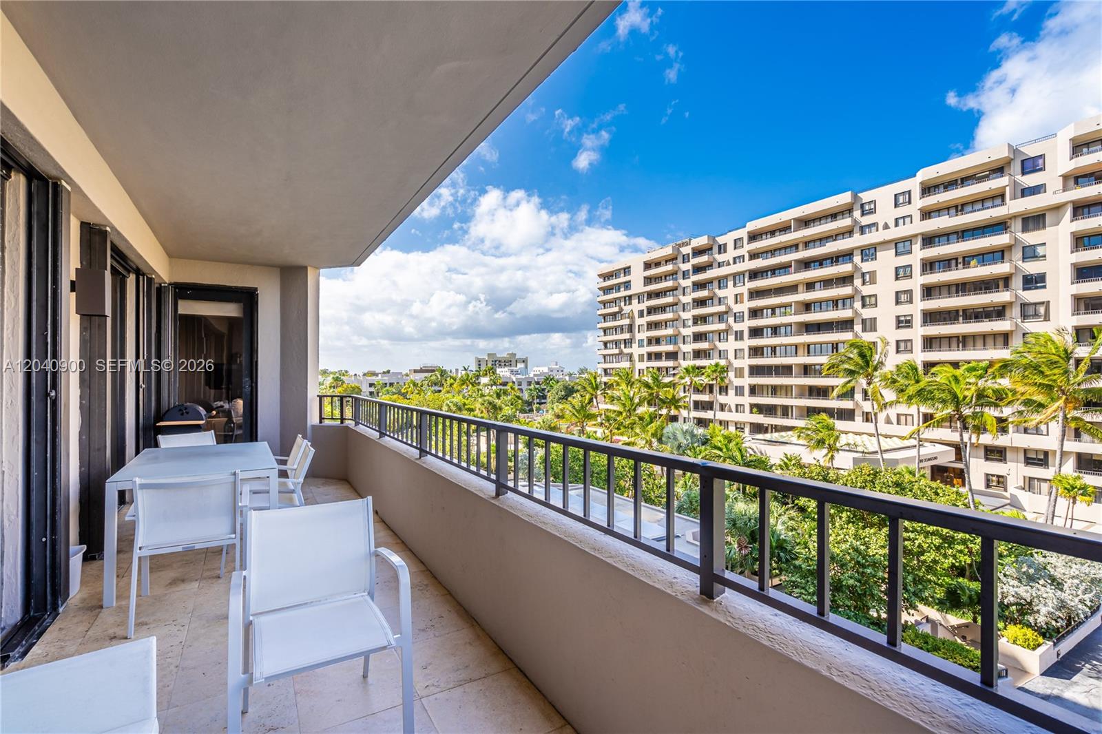A balcony with white patio furniture overlooks a tropical landscape and a large apartment building — 201 Crandon Blvd # 530, Key Biscayne FL 33149, KEY BISCAYNE, FL