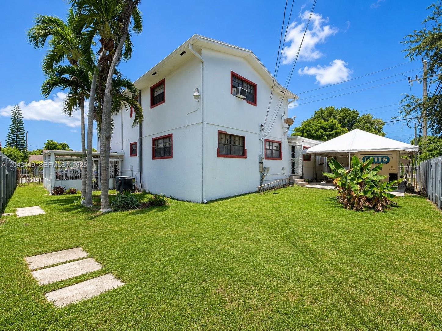 A two-story white house with red window trim stands in a grassy backyard — 1000 NW 47th St, Miami FL 33127, MIAMI, FL