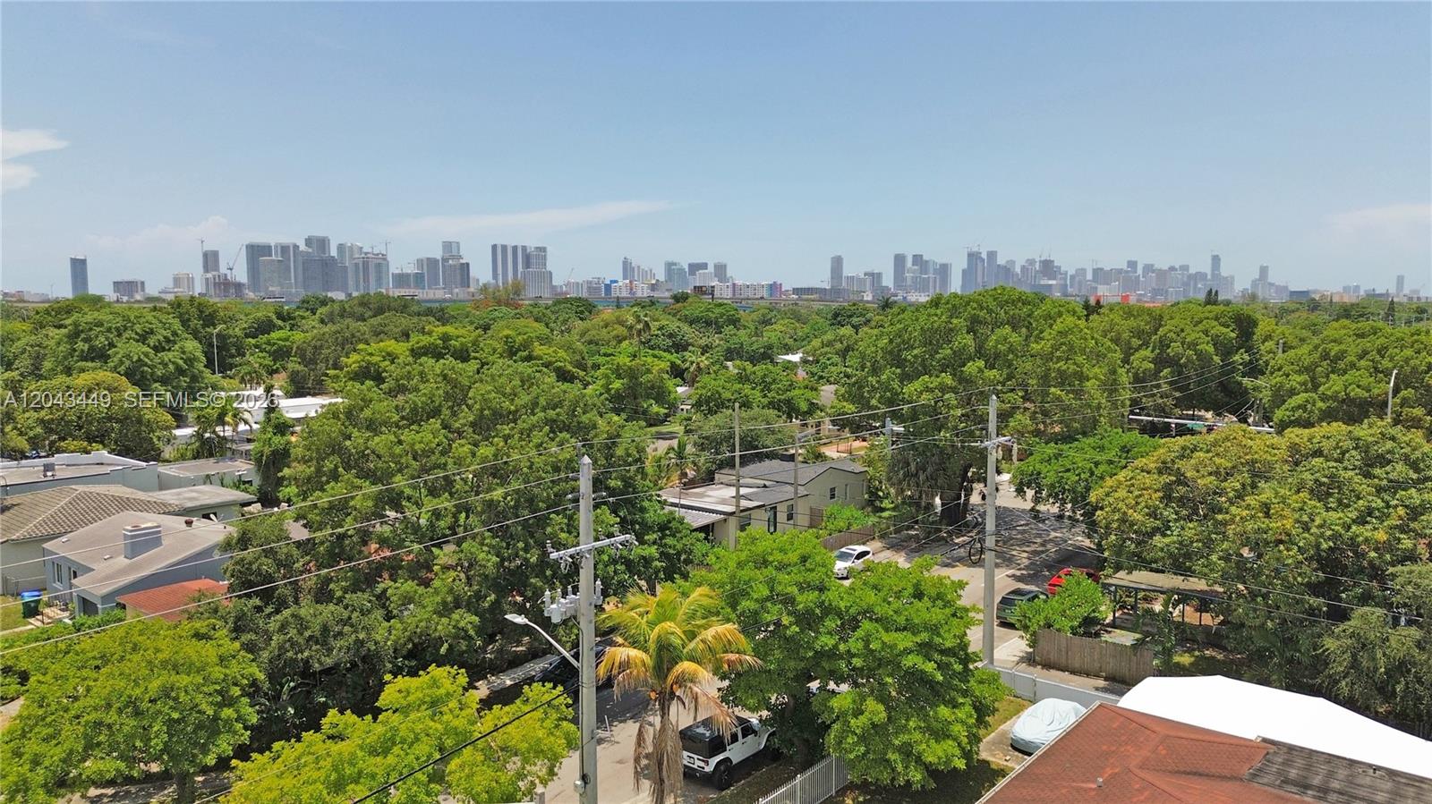 An elevated view shows a residential neighborhood with lush trees and a distant city skyline — 1000 NW 47th St, Miami FL 33127, MIAMI, FL