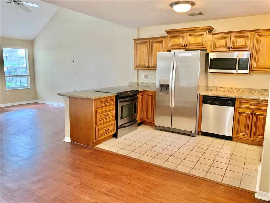 A kitchen with wood cabinets, stainless steel appliances, and tile flooring opens to a living area — 5268 SW 97TH WAY, GAINESVILLE, FL