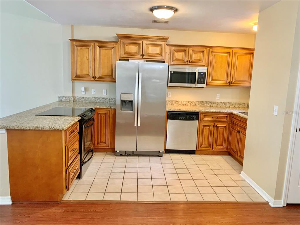 A kitchen features wood cabinets, granite countertops, stainless steel appliances, and a tiled floor — 5268 SW 97TH WAY, GAINESVILLE, FL