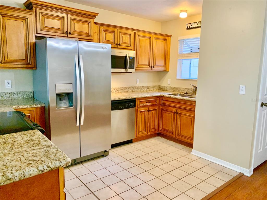 A kitchen features wood cabinets, stainless steel appliances, granite countertops, and a tiled floor — 5268 SW 97TH WAY, GAINESVILLE, FL