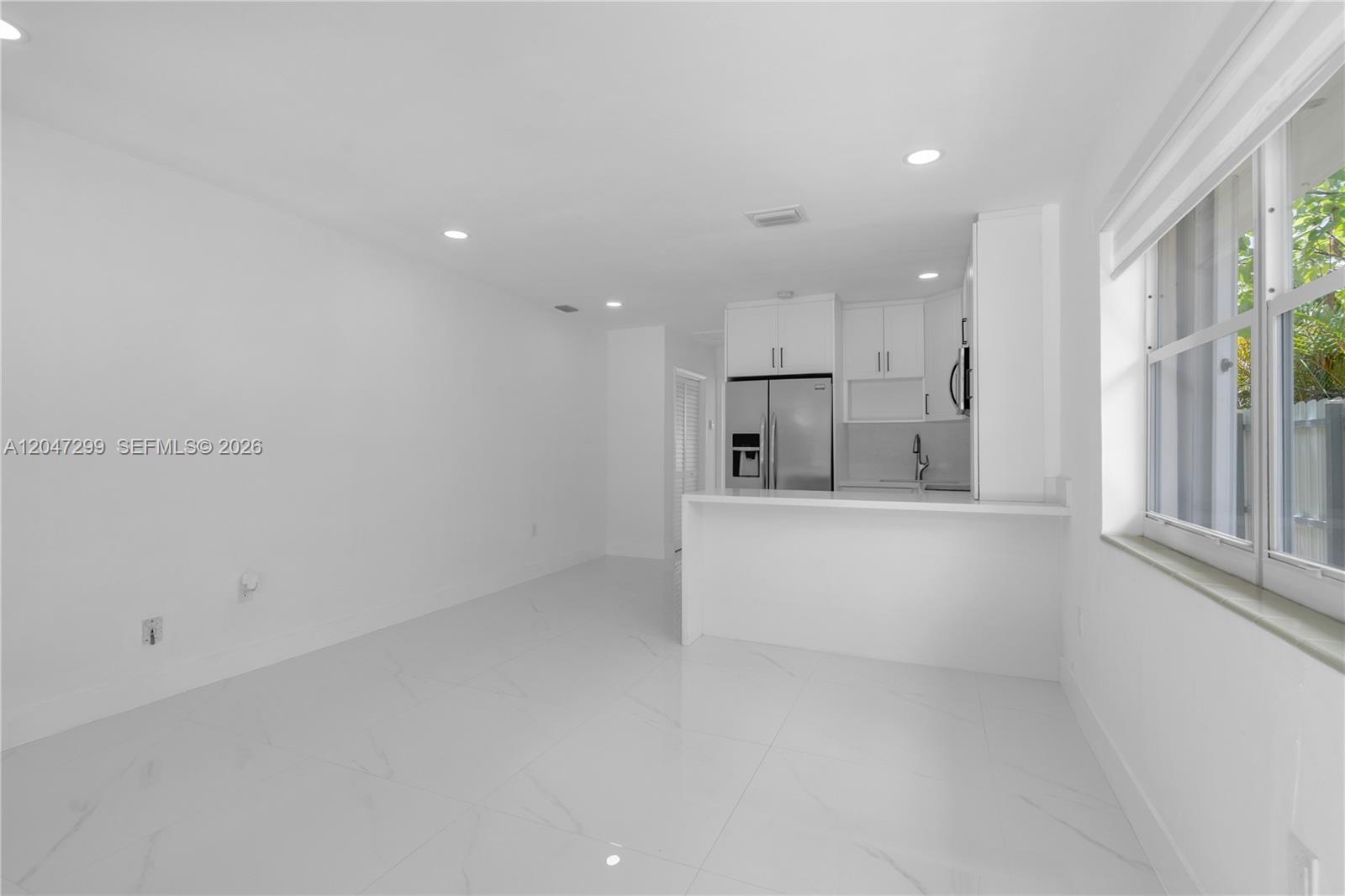 A bright, minimalist kitchen and dining area features white cabinetry, stainless appliances, and tile flooring — 2638 SW 30th Ct # 2638, Miami FL 33133, MIAMI, FL