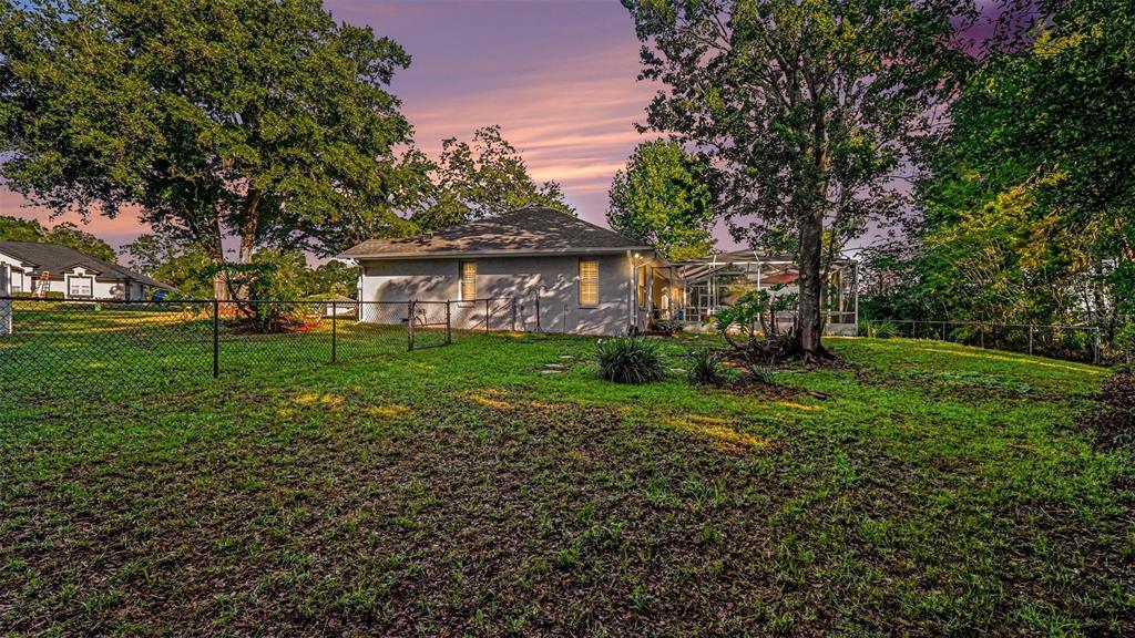 The backyard features a fenced lawn, mature trees, and a house with a screened patio — 6607 SE 11TH LOOP, OCALA, FL